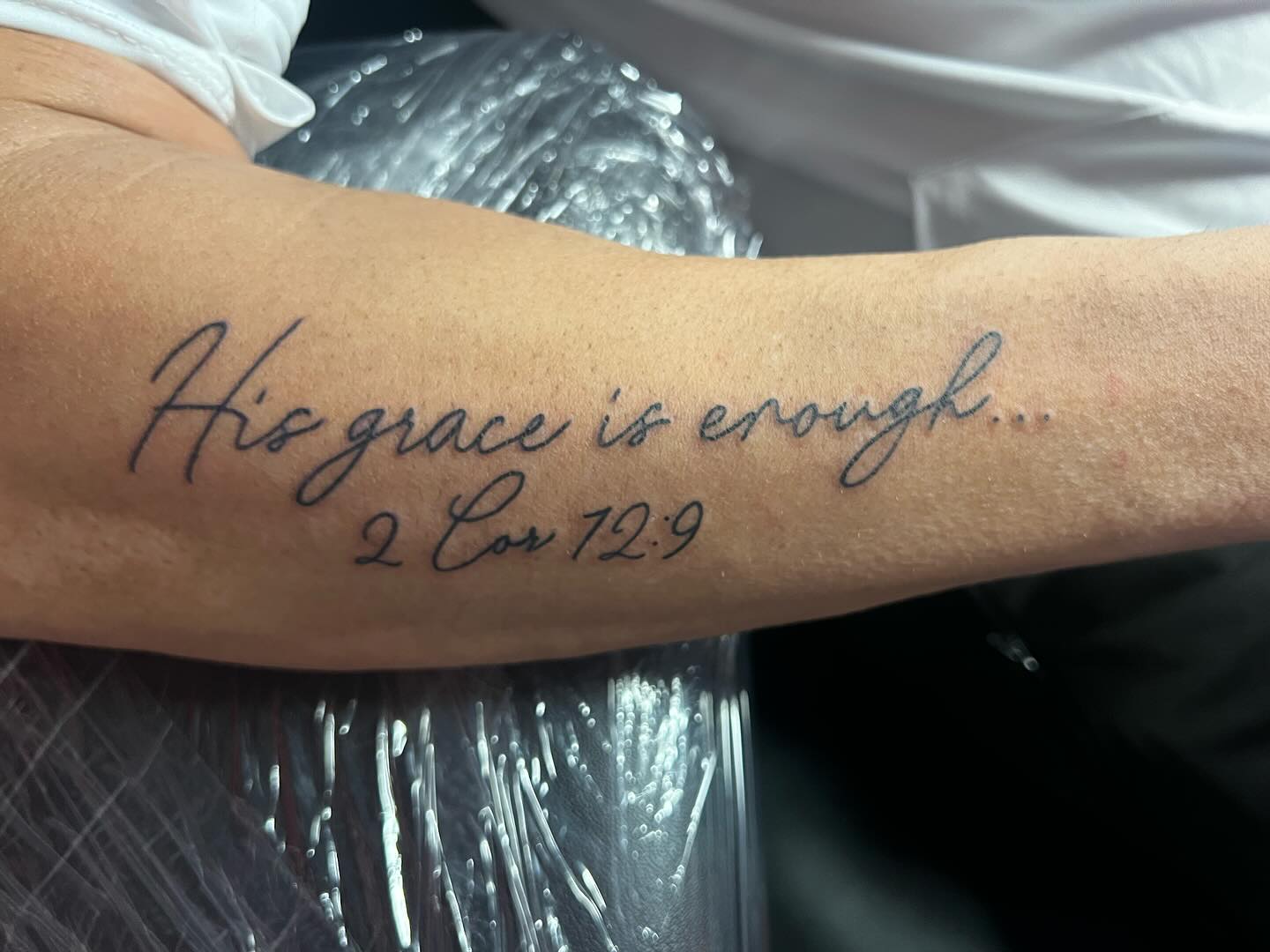 Fine line tattoo Bible verse in a handwritten style saying, "His grace is enough..."
